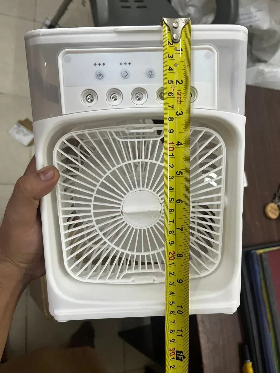 Small appliance with a fan visible, held by a hand with a tape measure for scale.