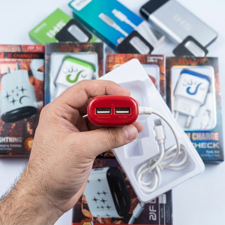 Hand holding a red USB charger with packaging of electronic accessories in the background