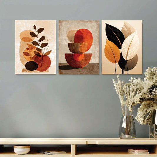 Three abstract art pieces on a wall with a vase of dried flowers below.